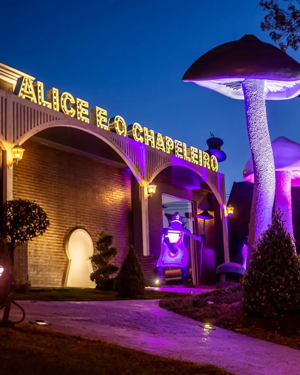 Fachada iluminada de Alice e o Chapeleiro com cogumelos cenográficos