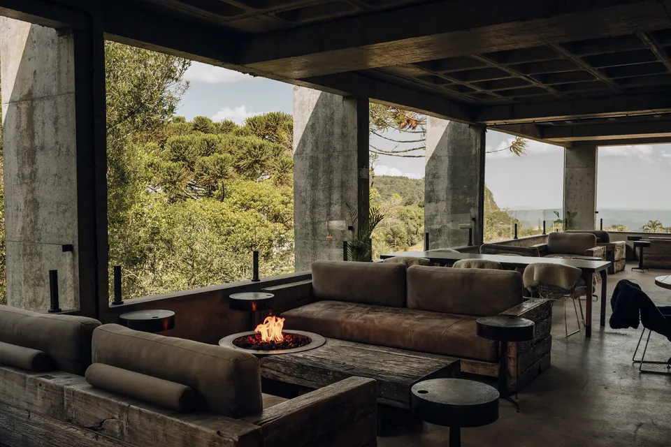 Lounge externo com lareira acesa e sofás de couro do restaurante 1835 Carne e Brasa no Kempinski Laje de Pedra em Canela, com vista panorâmica para as araucárias e o vale.